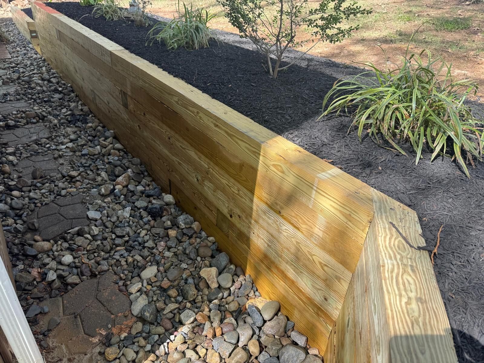 Wood retaining wall with river rock drainage and fresh mulch